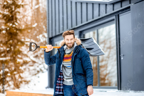 Wall Mural Portrait of a man in winter clothes with a snow shovel near the modern house in