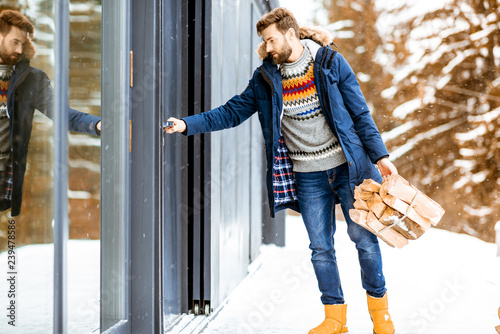 Man in winter clothes entering home carrying firewoods in the mountains