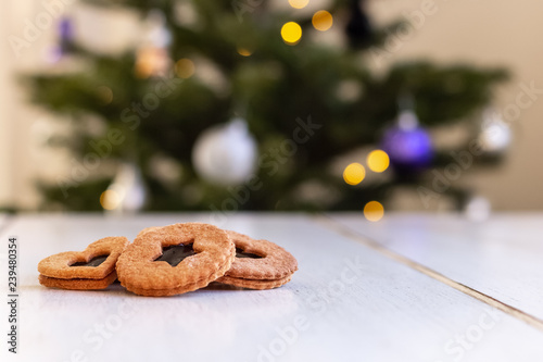 Homemade wholemeal Christmas cookies on a wooden table with a decorated Christmas tree in blurry background
