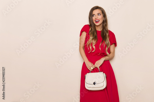 Smiling Beautiful Woman In Red Dress With Beige Purse Is Looking Away And Talking