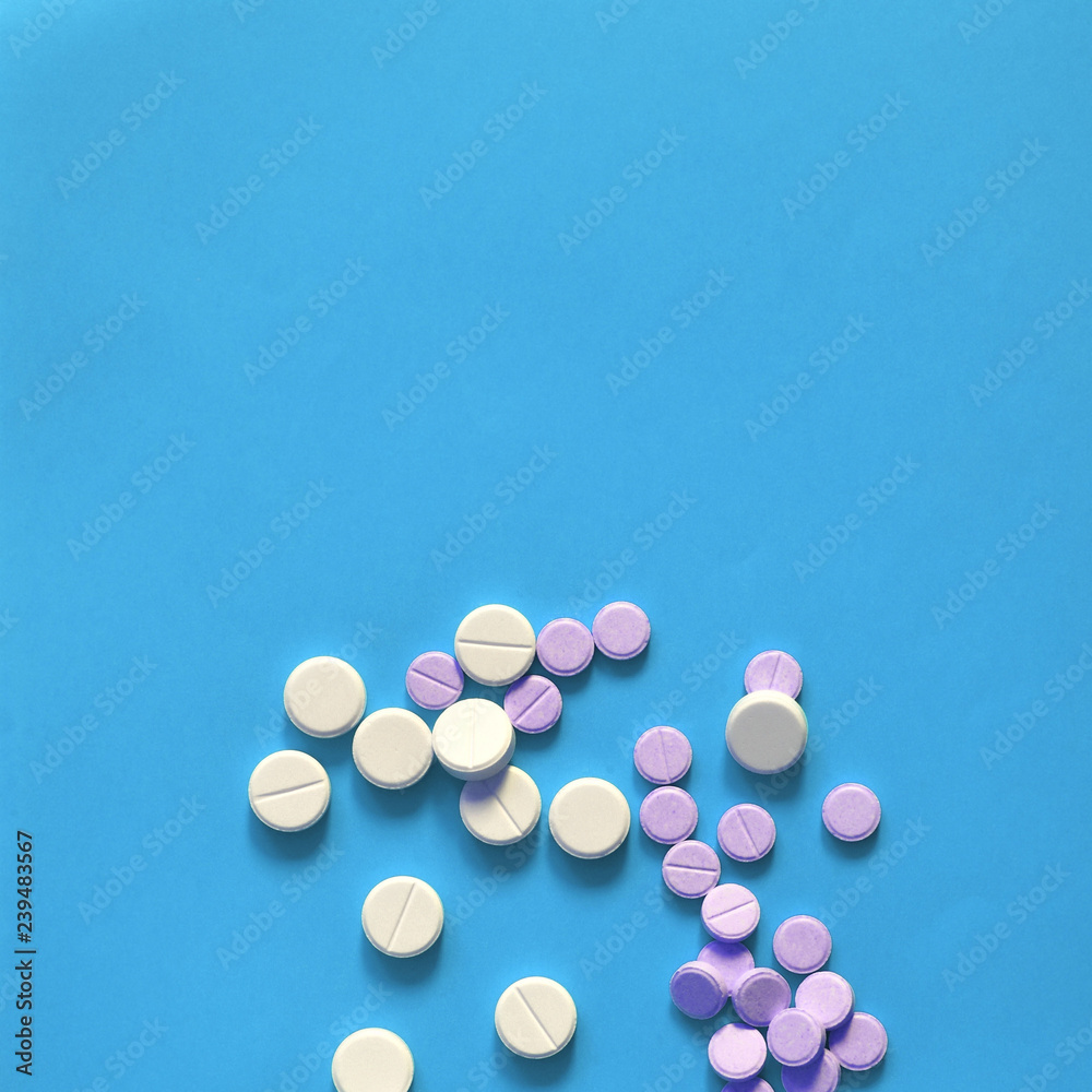 Pink and white pills scattered on a blue background. Copy space for text