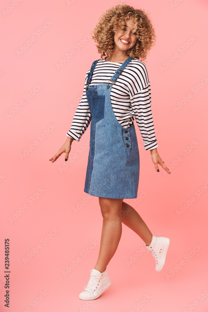Full length image of gorgeous curly woman 20s wearing casual clothes smiling while, isolated over pink background Full length image of gorgeous curly woman 20s wearing casual clothes smiling while, isolated over pink background