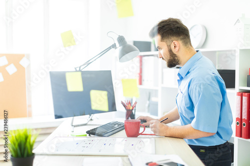 A young man stands in the office near a transparent Board with stickers.