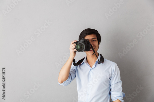 Happy asian man standing isolated over gray