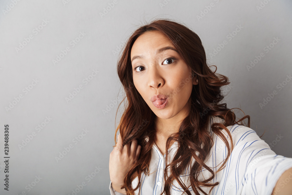 Fototapeta premium Cheerful asian woman standing isolated over gray