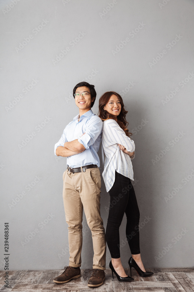 Full length of cheerful asian couple standing back to back Full length of cheerful asian couple standing back to back