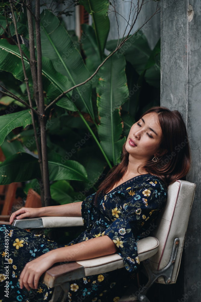 Fototapeta premium Beautiful asian woman keeping head on the grey wall while taking nap on comfortable barber chair. fashion tropical concept.
