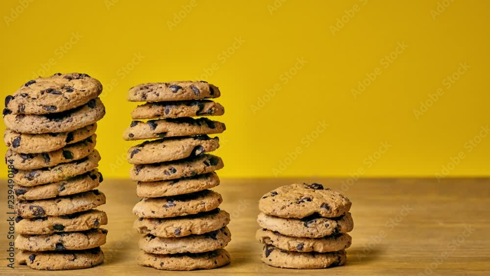 Homemade chocolate cookies are piled on a wooden table, yellow background