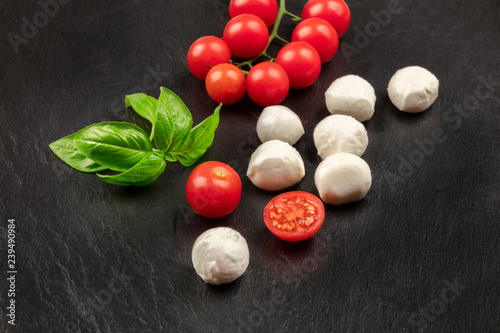 Mozzarella cheese balls with fresh basil leaves and cherry tomatoes, the ingredients of the Italian Caprese salad, on a black background with copy space