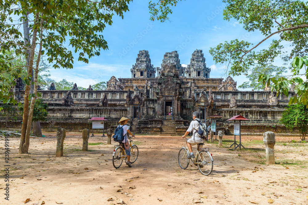 Fototapeta premium Tourist couple cycling around Angkor temple, Cambodia. Ta Keo building ruins in the jungle. Eco friendly tourism traveling.