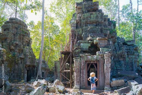 One tourist visiting Angkor ruins amid jungle, Ta Nei temple, travel destination Cambodia. Woman with traditional hat, rear view. photo