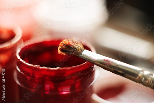 a jar of scarlet gouache and a fluffy brush for drawing lit by the bright sun photo