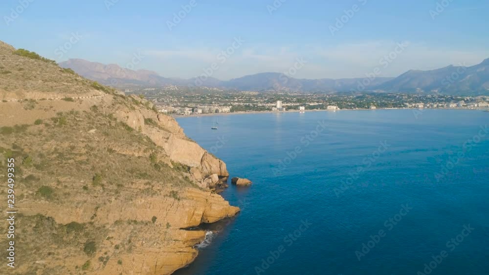 Aerial cinematic view, flying up slow above blue sea, big yellow rocky mountain coastline, yachts and city view at sunset sunrise golden hour time. Beautiful summer autumn view and soft light Aerial cinematic view, flying up slow above blue sea, big yellow rocky mountain coastline, yachts and city view at sunset sunrise golden hour time. Beautiful summer autumn view and soft light