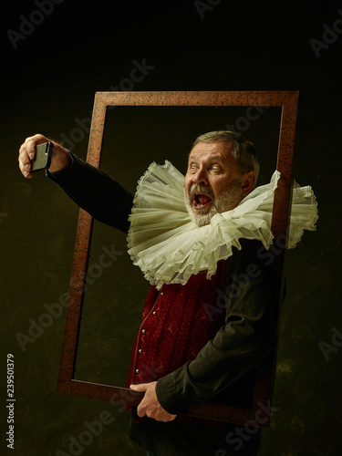 Official portrait of historical governor man with mobile phone from the golden age with corrugated round collar. Studio shot against dark wall. He making selfie photo photo