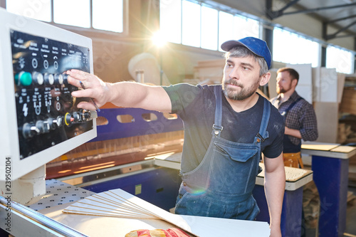 Fotografie Serious concentrated handsome gray-haired workman in cap and denim overall pushi