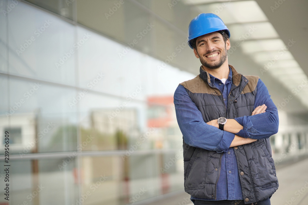 Smiling industrial worker in hardhat infront of modern building Smiling industrial worker in hardhat infront of modern building