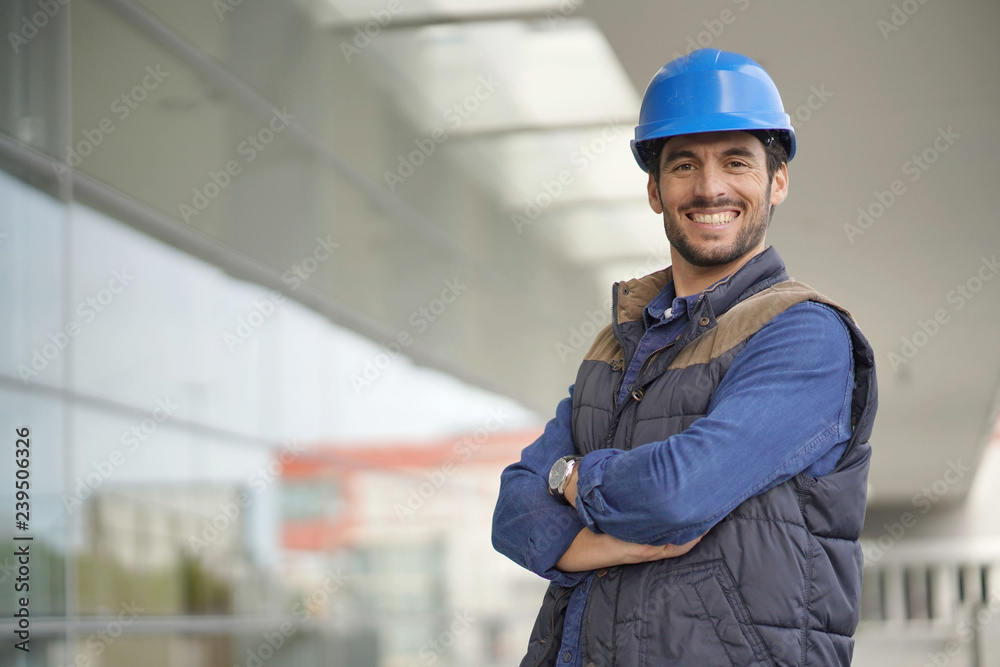 Smiling industrial worker in hardhat infront of modern building Smiling industrial worker in hardhat infront of modern building
