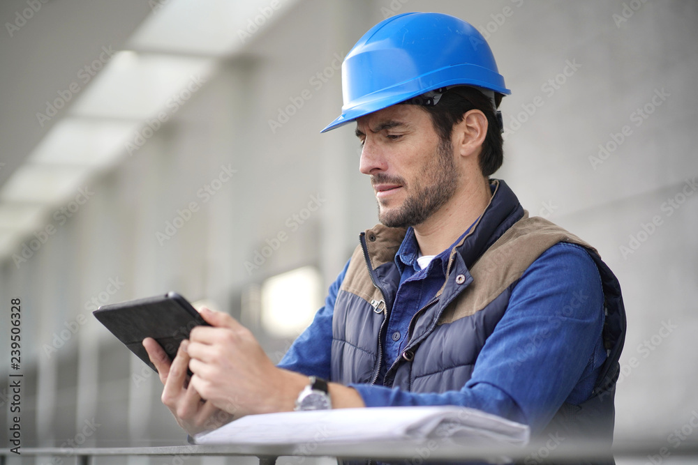 Handsome building expert in hardhat outdoors with tablet and blueprint Handsome building expert in hardhat outdoors with tablet and blueprint