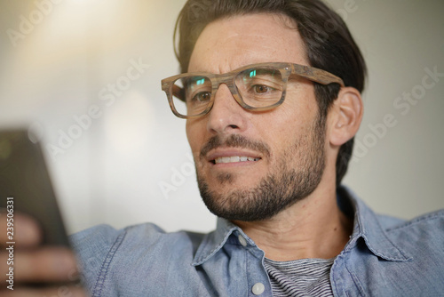Fototapeta Naklejka Na Ścianę i Meble -  Portrait of casual handsome man checking cellphone and wearing designer glasses