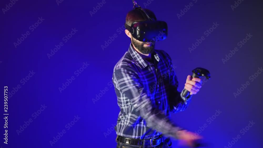 Man play 3D virtual reality game at the Metaverse. Waving swords with controllers in VR game. Man wearing VR headset on blue background Man play 3D virtual reality game at the Metaverse. Waving swords with controllers in VR game. Man wearing VR headset on blue background