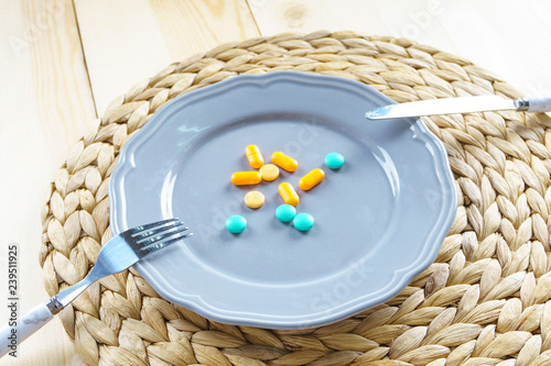 Top view of colourful medicine pills and capsules in white plate on country style background. Fork and knife. Diet pills and supplements. Healthy lifestyle concept photo