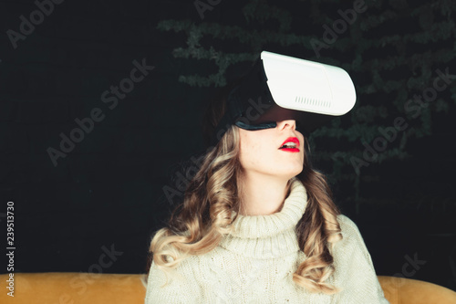Beautiful young girl wearing a virtual reality helmet and watching an online movie or playing a game at home. Model is experiencing strong emotions. Face close-up
