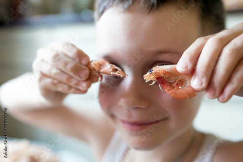 Little boy puts two shrimp to his eyes like glasses and smiles
