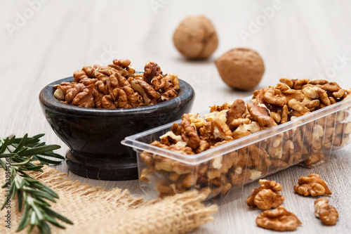 Walnuts in stone bowl and plastic container on a wooden background.