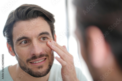 Handsome man checking wrinkles in mirror at home