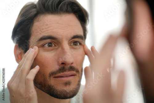 Handsome man checking wrinkles in mirror at home photo