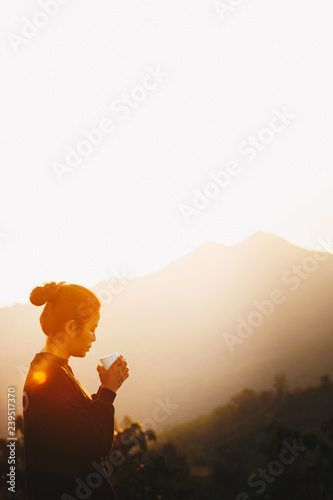 Asian Woman Standing drinking coffee and relaxing in sunrise and sunshine light enjoying life her warm morning on mountain  Lifestyle Concept