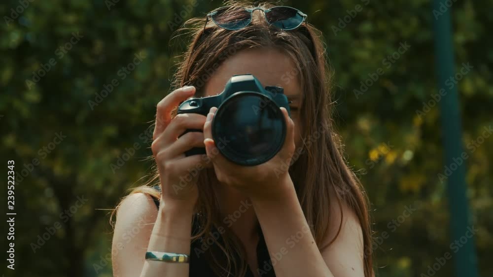 Woman photographer out in a sunlit park points her camera at the camera and snaps a picture Woman photographer out in a sunlit park points her camera at the camera and snaps a picture