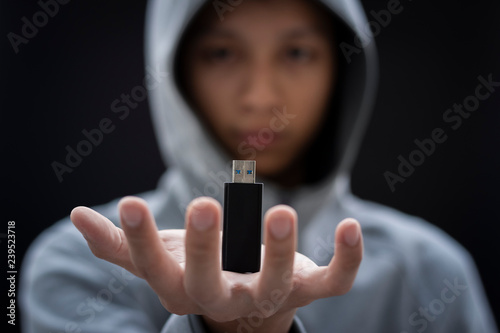 The man wears hoodie, hold his secret USB Flash Drive. Have black background.