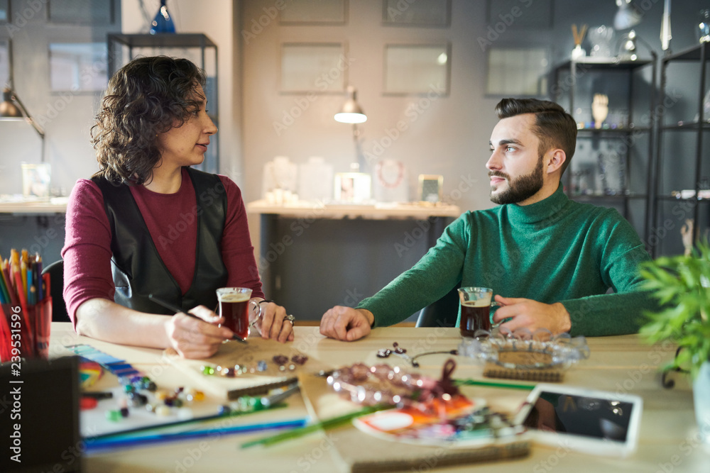 Portrait of handsome male designer discussing creative project while sitting at table with female colleague Portrait of handsome male designer discussing creative project while sitting at table with female colleague