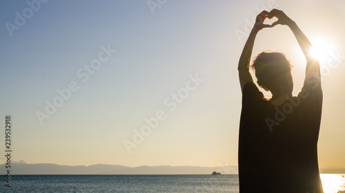 Woman hands in form of heart shape symbol framing sunset / sunrise on beach. Lifestyle, happiness, feelings concept. Magic, yoga, falling in love, meditation conceptual image. Girl making heart sign.