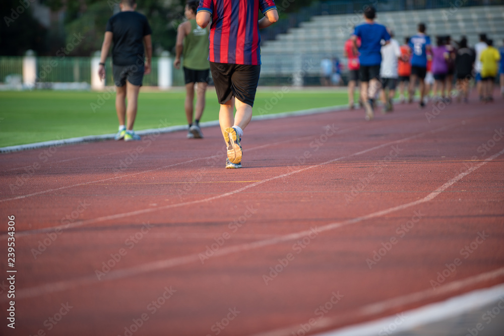 Groups of jogging people, with a variety of ages and sizes, running on the track in a stadium during the evening time with sun set.