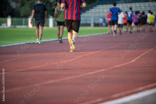 Groups of jogging people, with a variety of ages and sizes, running on the track in a stadium during the evening time with sun set.