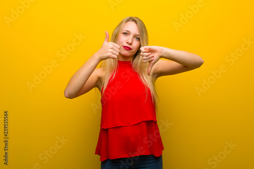 Young girl with red dress over yellow wall making good-bad sign. Undecided between yes or not