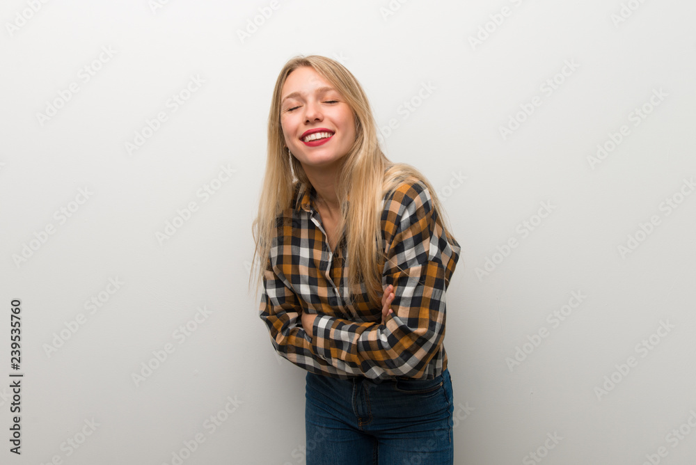Blonde young girl over white wall keeping the arms crossed while smiling Blonde young girl over white wall keeping the arms crossed while smiling