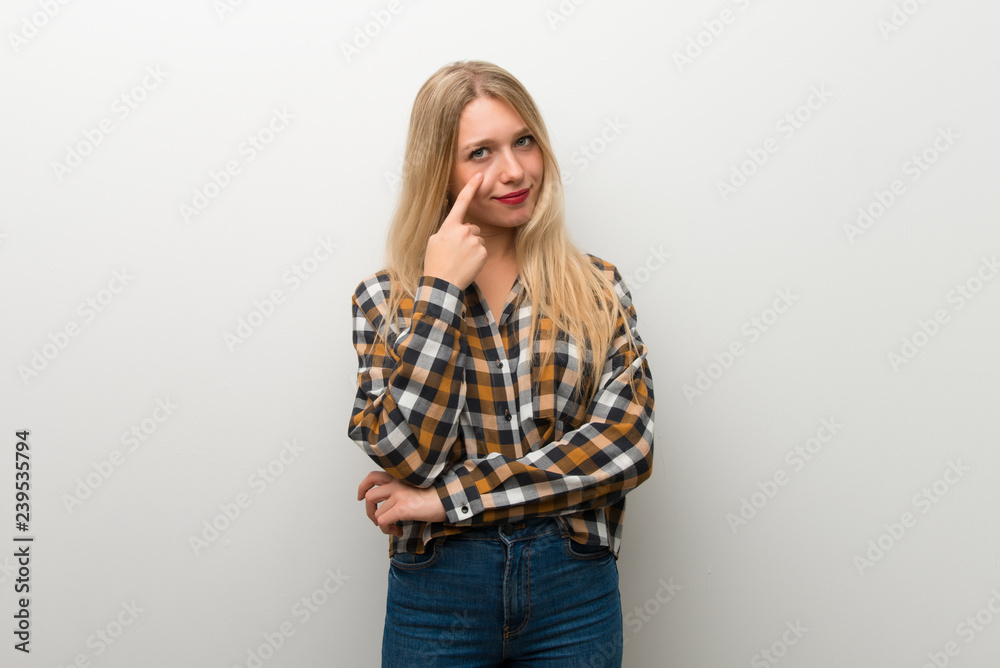 Blonde young girl over white wall looking to the front Blonde young girl over white wall looking to the front