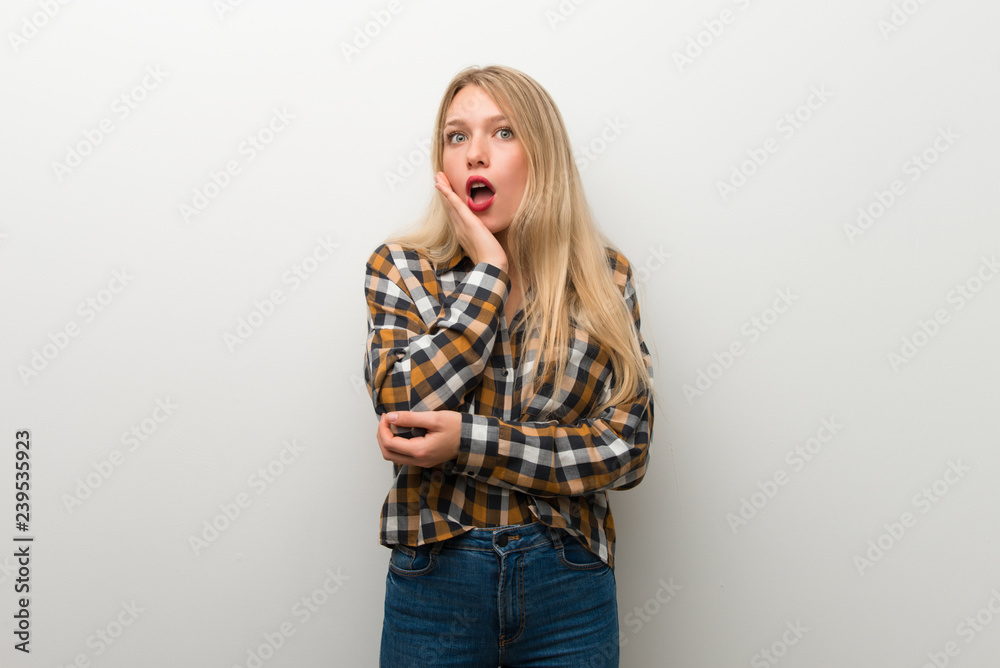 Blonde young girl over white wall surprised and shocked while looking right Blonde young girl over white wall surprised and shocked while looking right