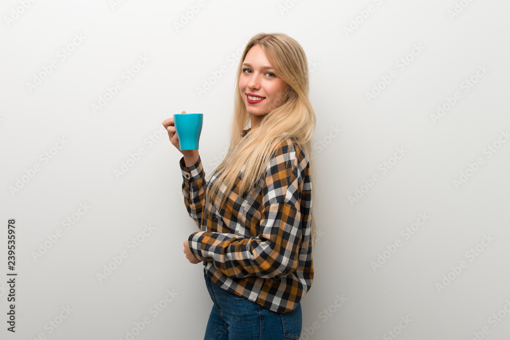 Blonde young girl over white wall holding a hot cup of coffee Blonde young girl over white wall holding a hot cup of coffee
