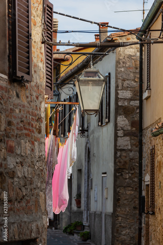 Narrow small street of medieval town Castiglione d'Orcia where between houses linen dries, Italy