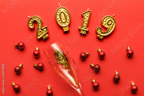 top view of champagne glass with golden confetti  2019 candles and red christmas baubles on red