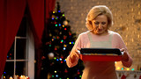 Retiree lady holding cooking dish with traditional biscuits, Xmas tree sparkling