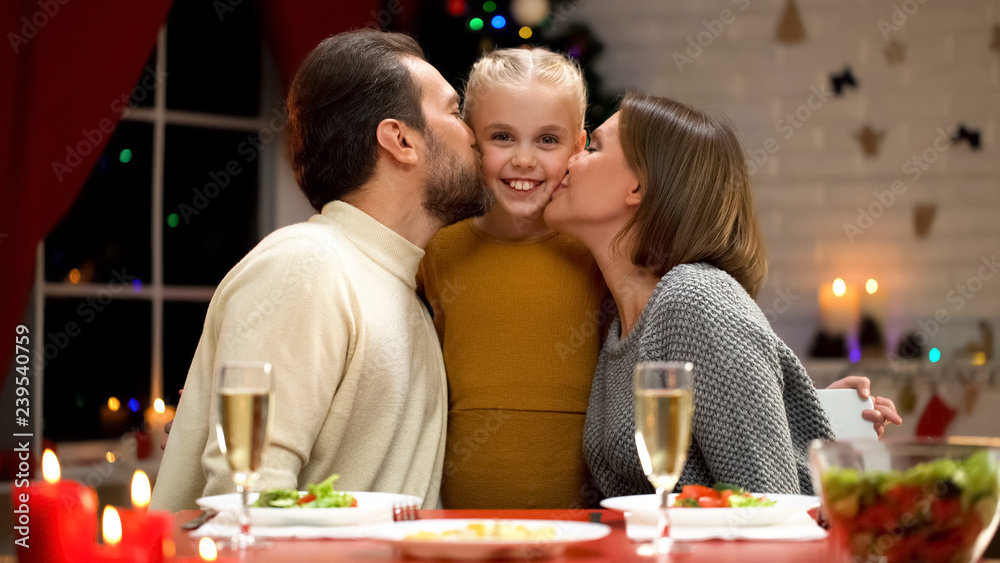 Happy parents kissing adorable daughter on Xmas eve, family celebrating holiday