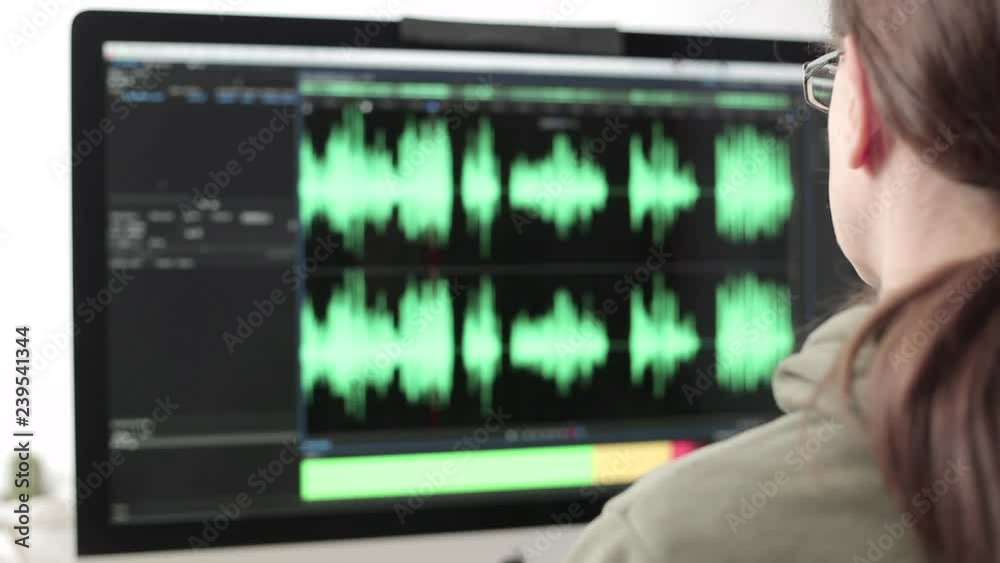 A woman works at the computer, edits the sound in the program. The monitor screen is unfocused. Workplace. A woman works at the computer, edits the sound in the program. The monitor screen is unfocused. Workplace.