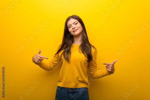 Teenager girl on vibrant yellow background proud and self-satisfied in love yourself concept