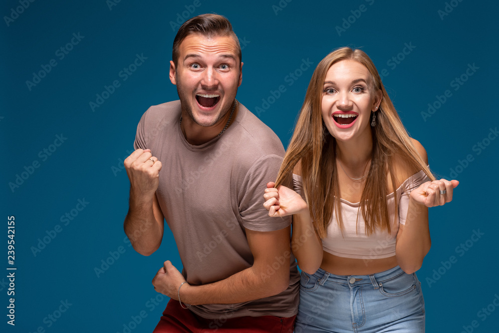 Obraz premium Overjoyed woman and man raise fists with triumph, have successful deal, exclaim joyfully, on blue background.