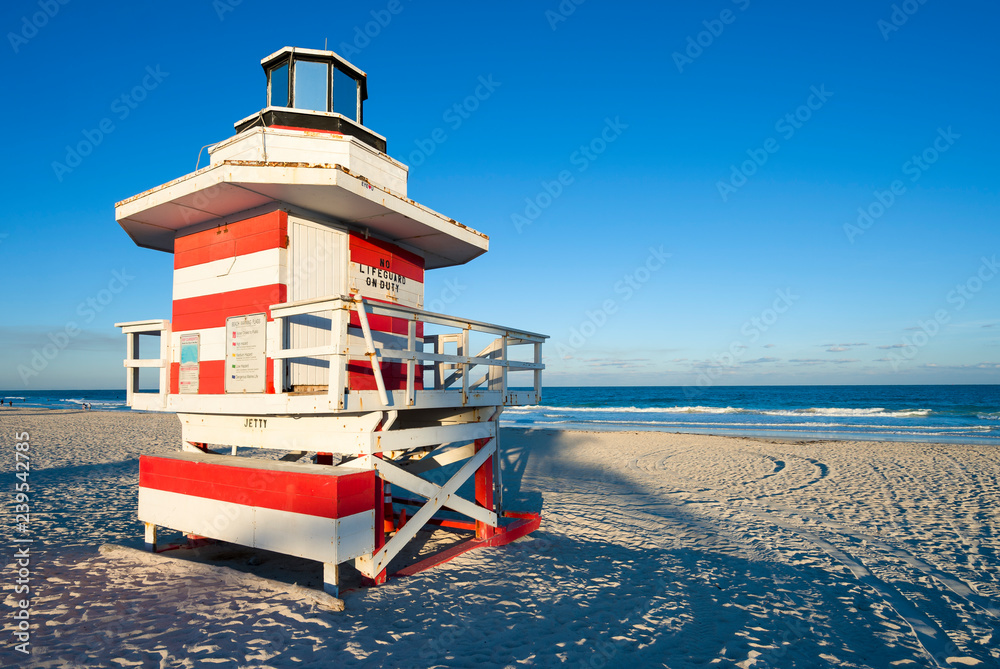 Fototapeta premium Scenic afternoon view of a classic wooden lifeguard tower painted in red and white stripes with sunset shadows in South Beach, Miami, Florida, USA